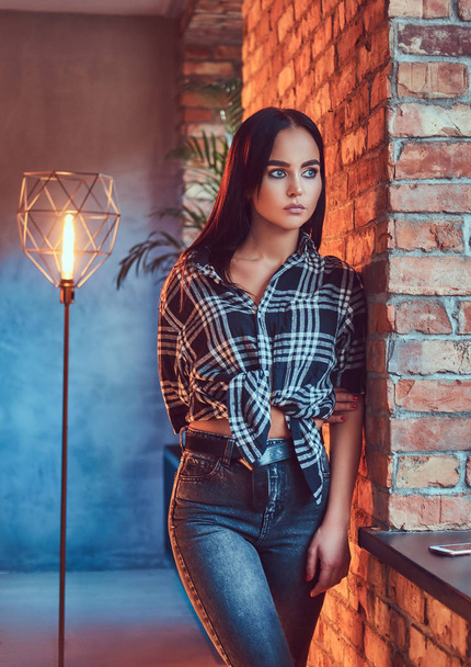 Portrait of an attractive hipster girl wearing flannel shirt leaning on the wall in a room with loft interior. - Foto, Bild