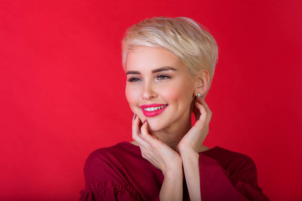 beautiful young girl with snow-white smile and healthy teeth with short hairdo on red background - Foto, Bild