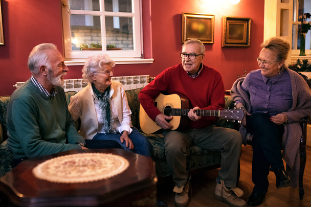 Old senior man playing guitar with his friends, making great par - Fotoğraf, Görsel