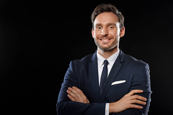 Guapo hombre de negocios inteligente en un traje de oficina clásico y corbata sosteniendo sus manos cruzadas con una sonrisa aislada sobre un fondo negro
 - Foto, imagen