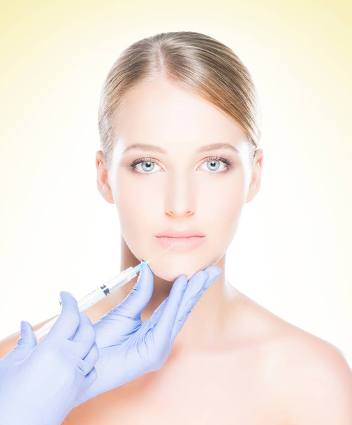 Young, beautiful and healthy woman having skin injections over yellow background. Plastic surgery concept. - Фото, зображення