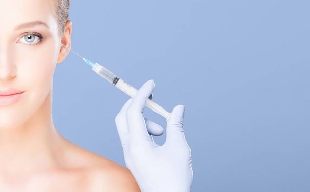 Young and beautiful woman having skin injections over blue background. Plastic surgery concept. - Fotó, kép