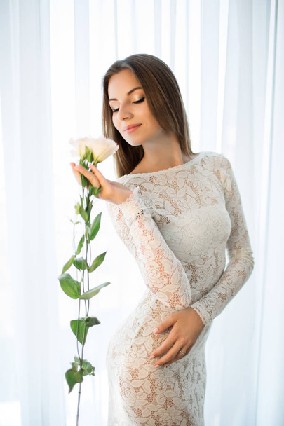 A girl in a white dress is enjoying the scent of a flower. - Fotoğraf, Görsel
