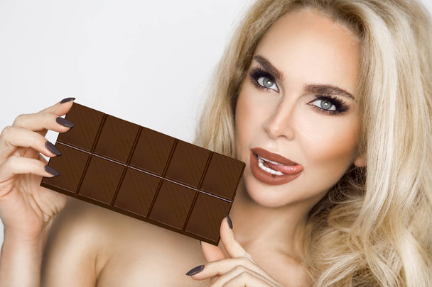 Όμορφη, σέξι ξανθιά, αισθησιακά τρώει σοκολάτα. - Φωτογραφία, εικόνα