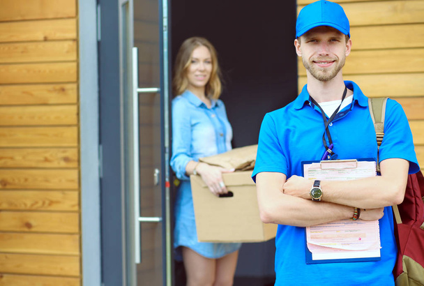 Smiling delivery man in blue uniform delivering parcel box to recipient - courier service concept. Smiling delivery man in blue uniform - Foto, imagen
