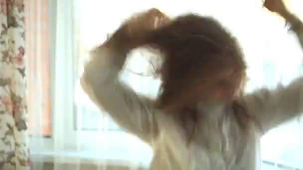 Mädchen lockiges Haar, dreht aktiv den Kopf, wedelt mit den Händen, springt, spielt, hört Musik über Kopfhörer am Fenster, tanzt, singt. Porträt - Filmmaterial, Video