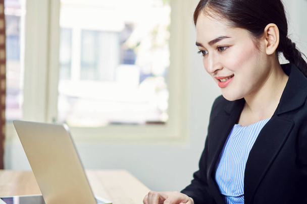 Eine lächelnde Geschäftsfrau im schwarzen Anzug sitzt am Laptop im Büro. Glückliches Arbeitskonzept. - Foto, Bild