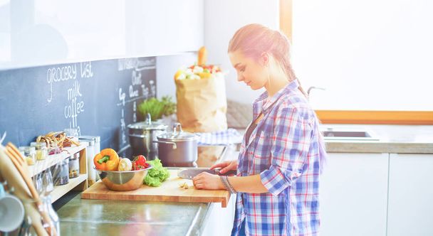 Young woman cutting vegetables in kitchen near desk - Photo, image