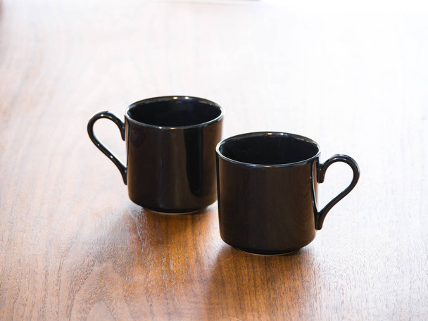 Lähikuva näkymä kaksi musta posliini tai keraaminen teetä tai kahvia kuppeja tai mukeja eristetty tumma puu viljan pöytä ja puoli sydämen muotoinen kahvat
. - Valokuva, kuva