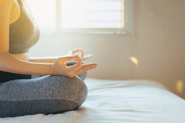 Young asian woman sitting on bed practicing doing yoga meditating,workout exercise after waking up in morning,Healthy and lifestyle concept - Photo, Image