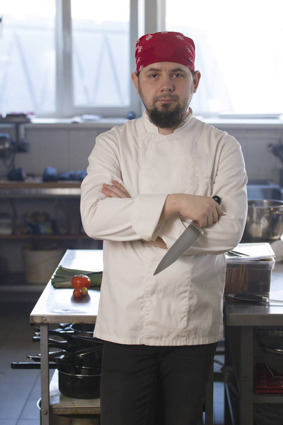 Retrato de un chef de moda en bandana sosteniendo un cuchillo en una cocina
 - Foto, Imagen
