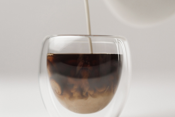 Verser le lait dans une tasse avec du café sur fond blanc
 - Photo, image