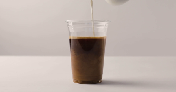 Выливание молока из кувшина в одноразовую чашку с черным кофе на белом фоне
 - Кадры, видео