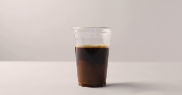 Verter la leche de la jarra en una taza de plástico con café sobre fondo blanco
 - Metraje, vídeo