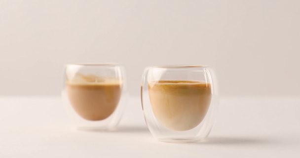 Versare il latte dalla brocca in una delle due tazze con caffè su sfondo bianco
  - Filmati, video
