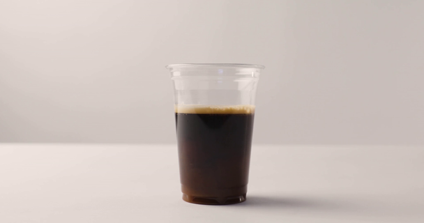 Pouring milk from jug in plastic cup with coffee on white background with reverse footage - Footage, Video