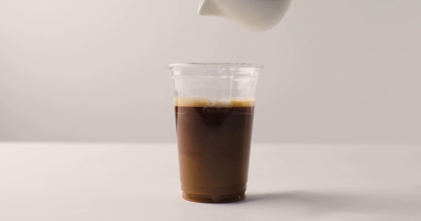 Man filling plastic cup of coffee with milk and lifting cup on white background with reverse footage - Footage, Video