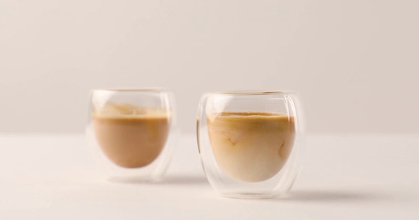 Verser le lait dans l'une des deux tasses avec du café sur fond blanc
 - Séquence, vidéo