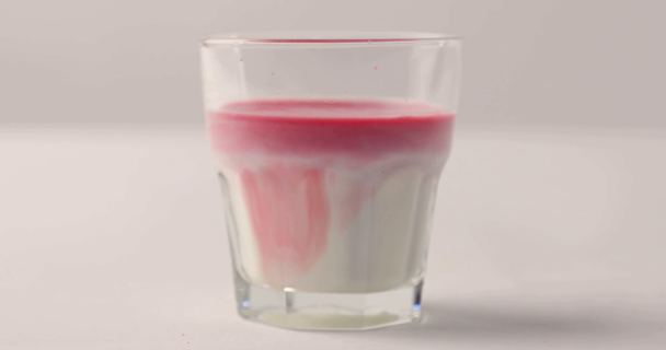 Nalévání červeného sirupu ve sklenici s mlékem na bílém pozadí - Záběry, video
