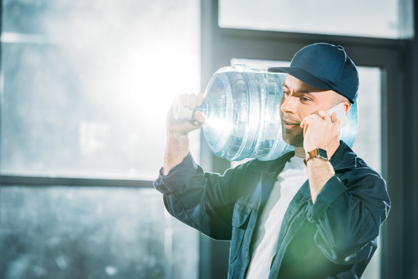 Poslíček přepravující láhev s vodou a mluví o telefonu - Fotografie, Obrázek