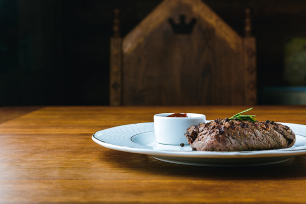 вкусный стейк на гриле с розмарином и соусом барбекю на тарелке на деревянном столе
 - Фото, изображение