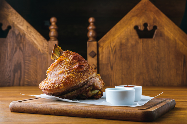 close-up view of delicious roasted pork knuckle with sauces on wooden tabletop - Fotografie, Obrázek