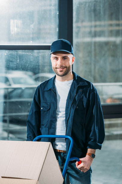 Smiling delivery man holding hand truck - Zdjęcie, obraz