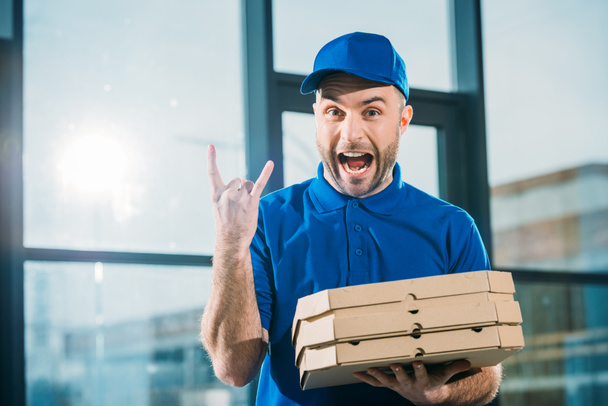 Emocionado mensajero con pizzas en cajas que muestran señal de roca
 - Foto, imagen