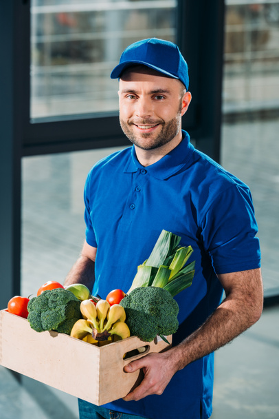 Delivery man holding box with fresh groceries - Foto, imagen