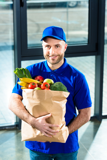 Delivery man holding paper bag with fresh fruits and vegetables - Foto, afbeelding