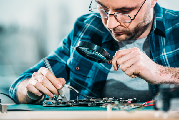 Engineer fixing circuit board looking through magnifying glass - Foto, Imagem