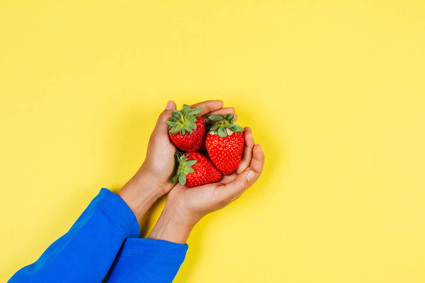 Kid hands holding fresh strawberries on yellow background - 写真・画像