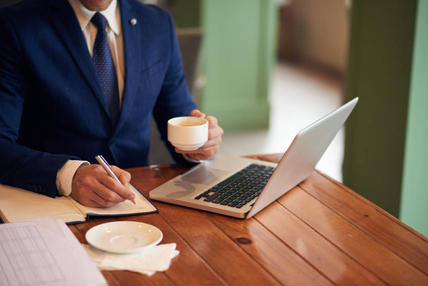 Обрезанный образ бизнес-руководителя, делающего заметки в его напоминании и пьющего крепкий кофе
 - Фото, изображение