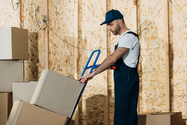 Loader man adjusting cardboard boxes on delivery cart - Foto, Bild
