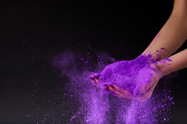 vista recortada de las manos femeninas con polvo de holi púrpura, aislado en negro
 - Foto, Imagen