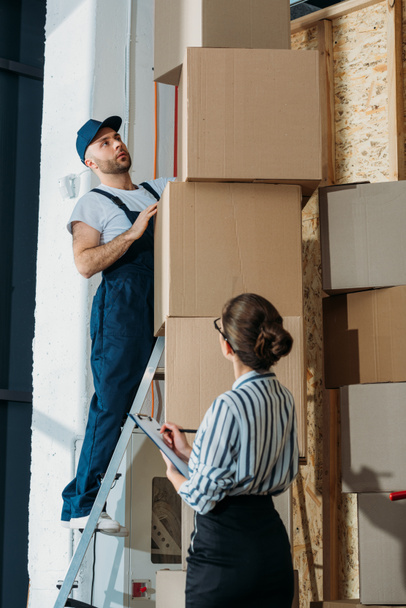 Businesswoman filling checklist while loader man standing on a ladder - Valokuva, kuva