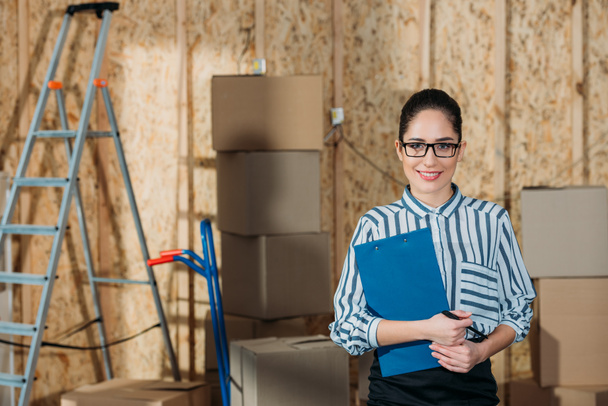 Smiling businesswoman holding clipboard standing near cargo boxes - Photo, Image