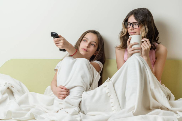 Girls teenagers are sitting at home in bed and watching TV. - Фото, изображение
