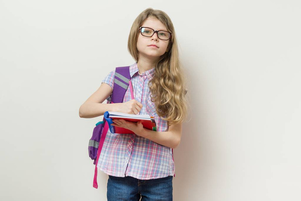 Young schoolgirl in glasses and with a backpack writes in a school notebook. - Φωτογραφία, εικόνα
