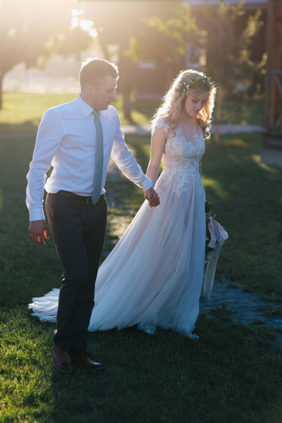 όμορφο γάμο νεαρό ζευγάρι κρατώντας τα χέρια και το περπάτημα στο πράσινο γκαζόν - Φωτογραφία, εικόνα