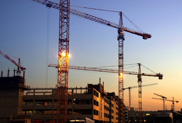 Construction of new homes. Silhouettes of cranes on the background of the evening sky. - Photo, Image