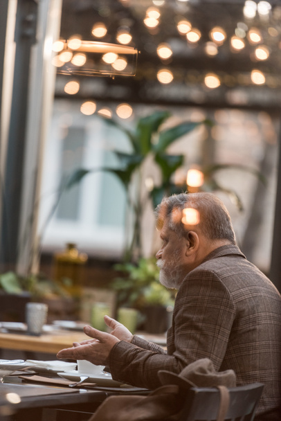 Widok z boku z starszy mężczyzna siedzący przy stole filiżankę kawy podczas spotkania w kawiarni - Zdjęcie, obraz