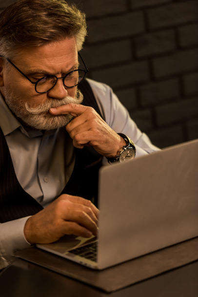 вид сфокусированного пожилого бизнесмена, работающего на ноутбуке в кафе
 - Фото, изображение