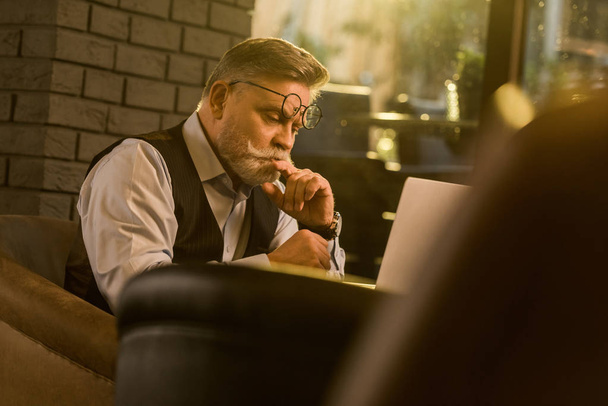 vista laterale di uomo d'affari anziano pensieroso che guarda lo schermo di computer portatile in caffè
 - Foto, immagini