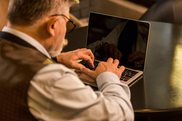 selective focus of senior businessman typing on laptop in cafe - Zdjęcie, obraz