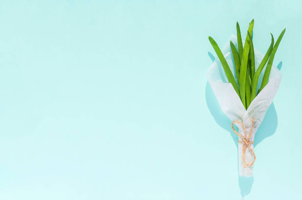 Buquê de folhas de cebola verde fresca em papel artesanal branco isolado em um fundo azul claro
 - Foto, Imagem