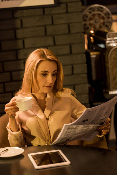 portrait of businesswoman with cup of coffee reading newspaper in cafe - Fotografie, Obrázek