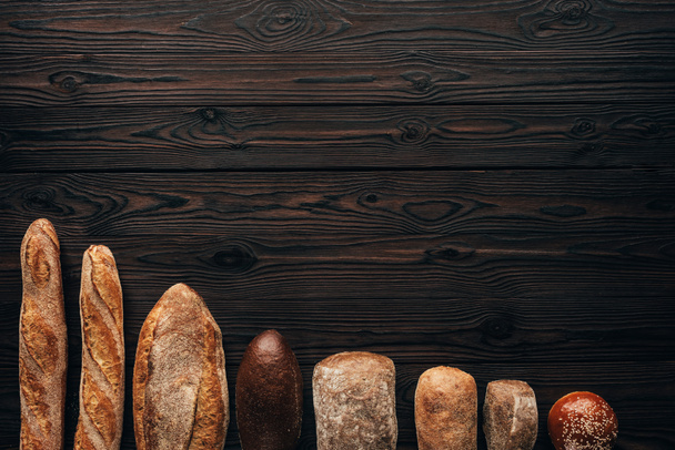top view of arranged loafs of bread on wooden surface - Photo, Image
