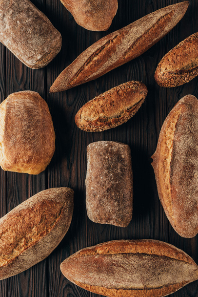 top view of arranged loafs of bread on wooden surface - Fotó, kép