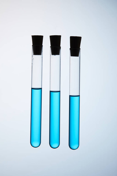 composición de tubos de ensayo llenos de líquido azul flotando en el aire sobre gris
 - Foto, Imagen